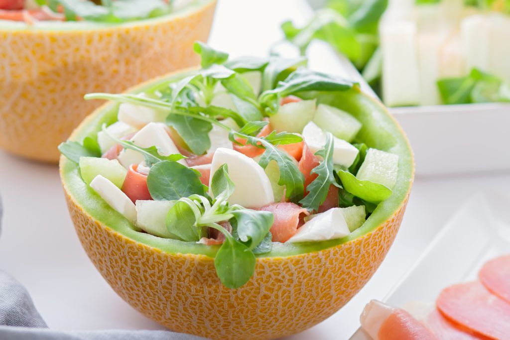 Summer mediterranean salad with ham and melon on white table top